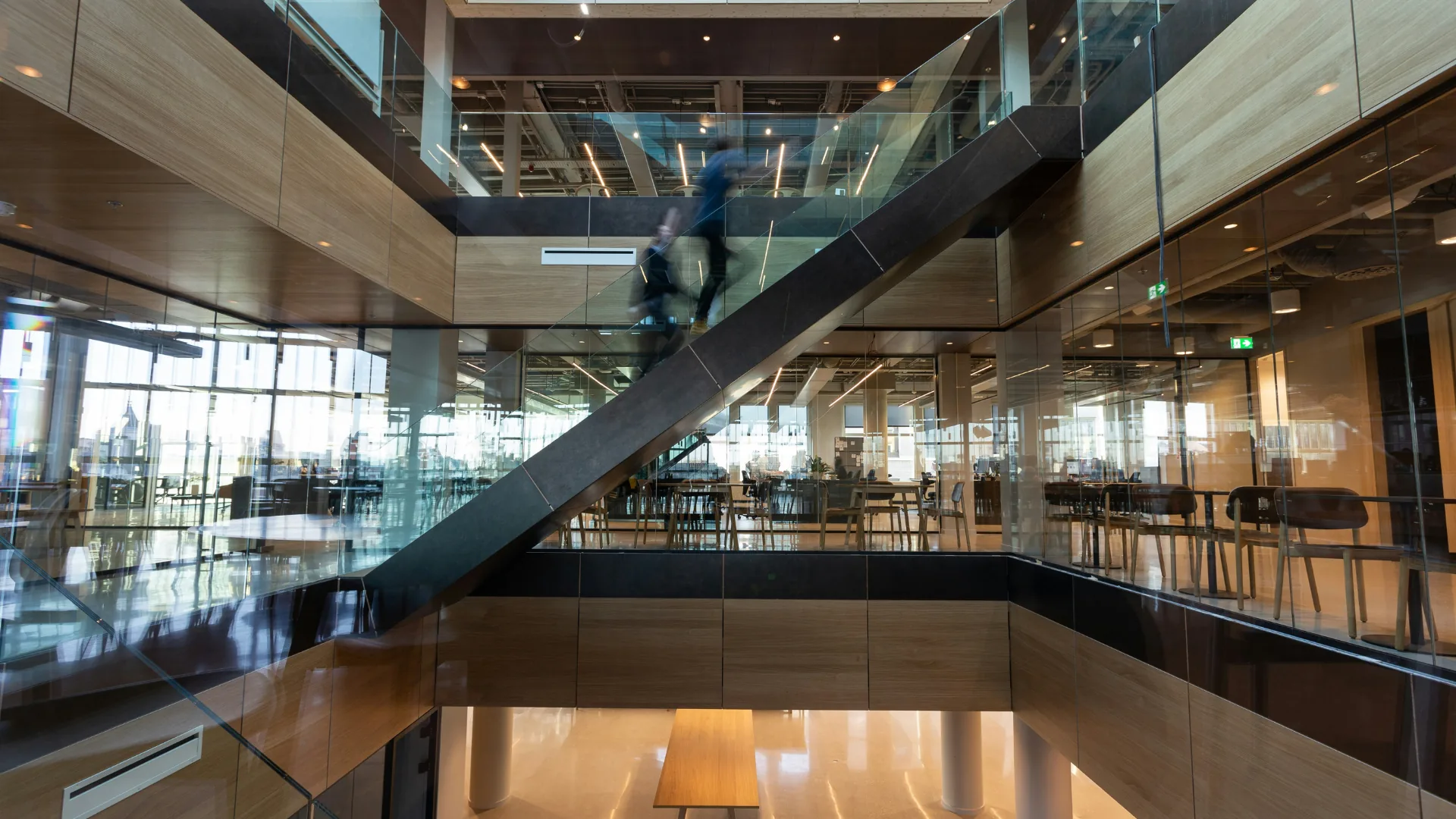 Wood and glass interior at an Elementa workspace, with a staircase and someone walking through